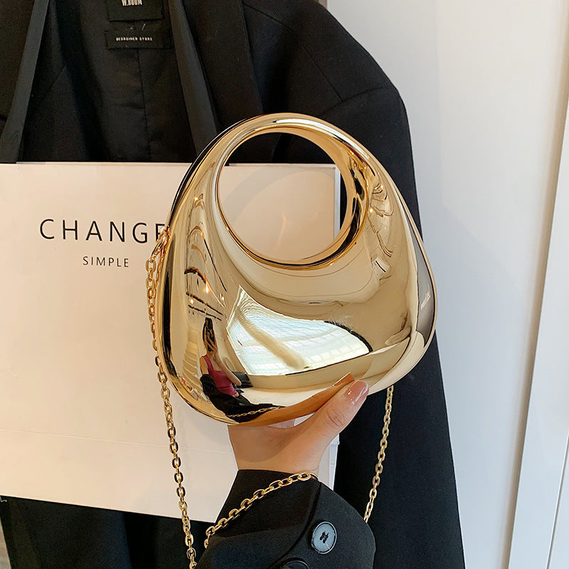 Front view of the Golden Eclipse handbag in a metallic gold finish. The bag has a unique crescent shape with a large circular handle cutout and a delicate gold chain strap. brand baazuu