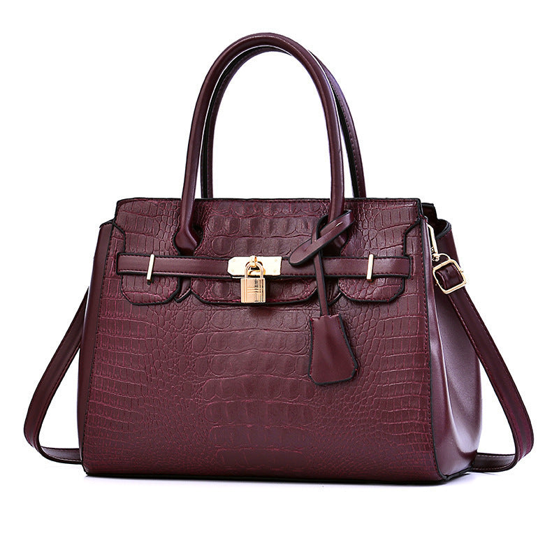 Maroon handbag with gold lock and strap on a white background
