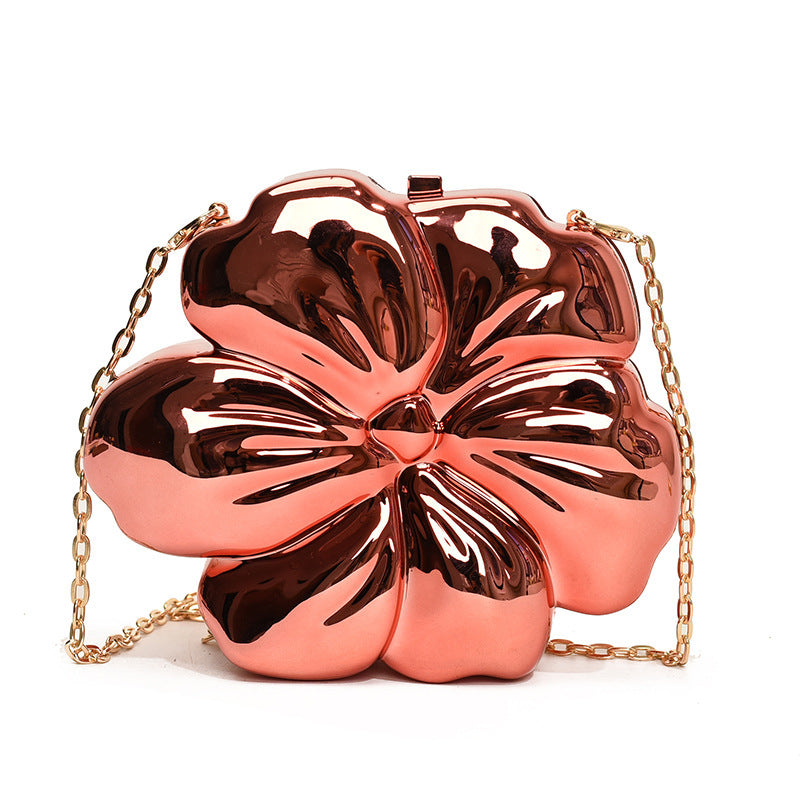 The Baazuu Bloom Bling floral clutch in a metallic red finish. This sculptural, flower-shaped handbag features a hard-shell design and a chain strap, perfect as a modern statement piece.
