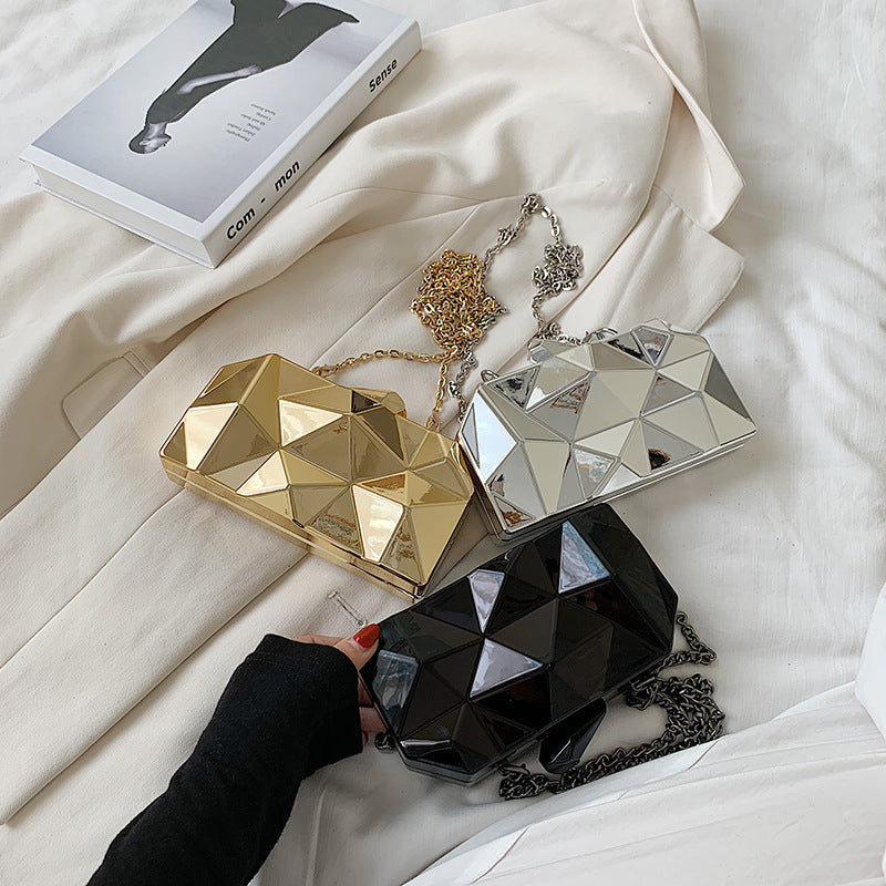 The Prism Aura geometric acrylic clutch shown in three colors: gold, silver, and black. This statement evening bag has a reflective, diamond-cut design and comes with a chain strap.