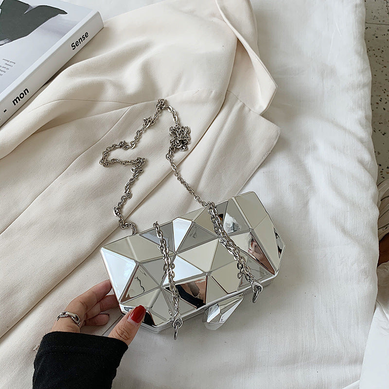 The Prism Aura geometric acrylic clutch shown in silver. This statement evening bag has a reflective, diamond-cut design and comes with a chain strap.