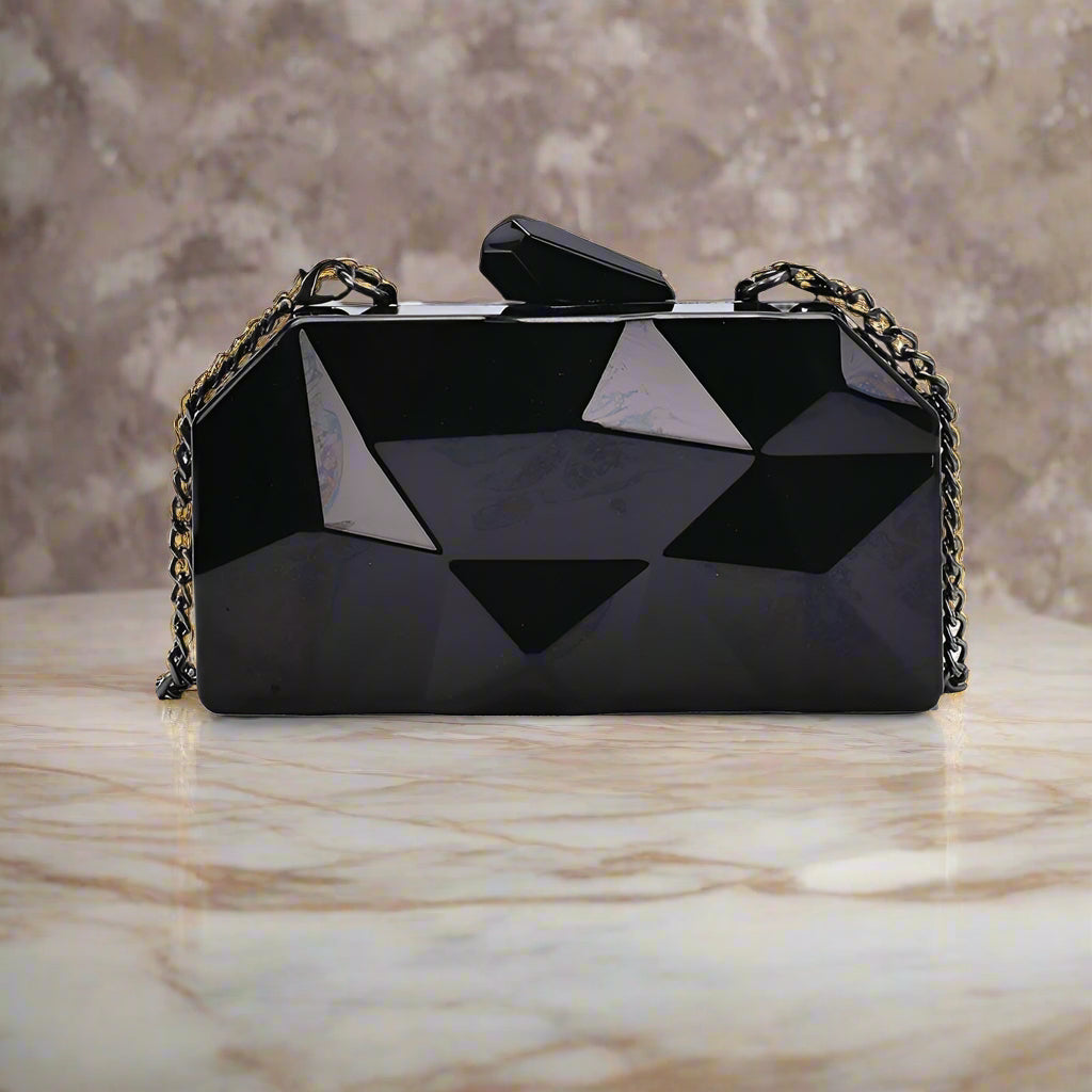 The Prism Aura geometric acrylic clutch shown in black color. This statement evening bag has a reflective, diamond-cut design and comes with a chain strap.