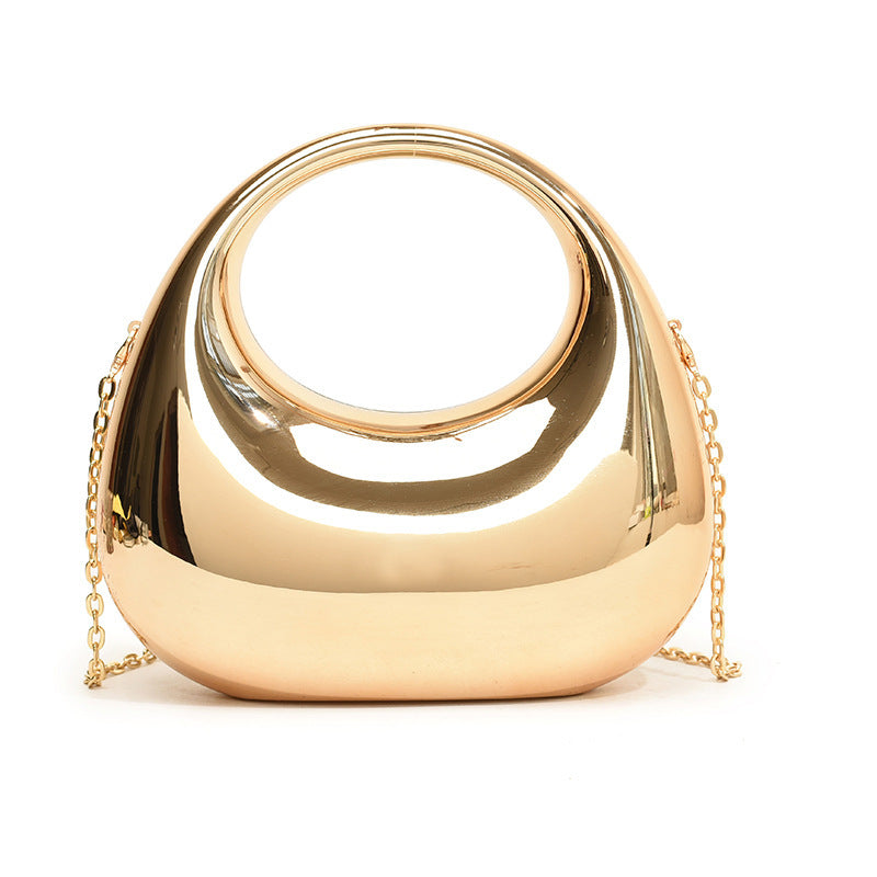 Front view of the Golden Eclipse handbag in a metallic gold finish. The bag has a unique crescent shape with a large circular handle cutout and a delicate gold chain strap. brand baazuu