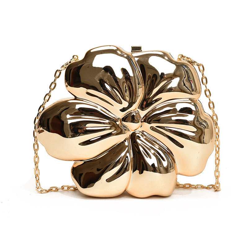 The Baazuu Bloom Bling floral clutch in a metallic gold finish. This sculptural, flower-shaped handbag features a hard-shell design and a chain strap, perfect as a modern statement piece.