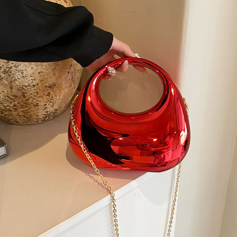 Front view of the Golden Eclipse handbag in a metallic red finish. The bag has a unique crescent shape with a large circular handle cutout and a delicate gold chain strap. brand baazuu