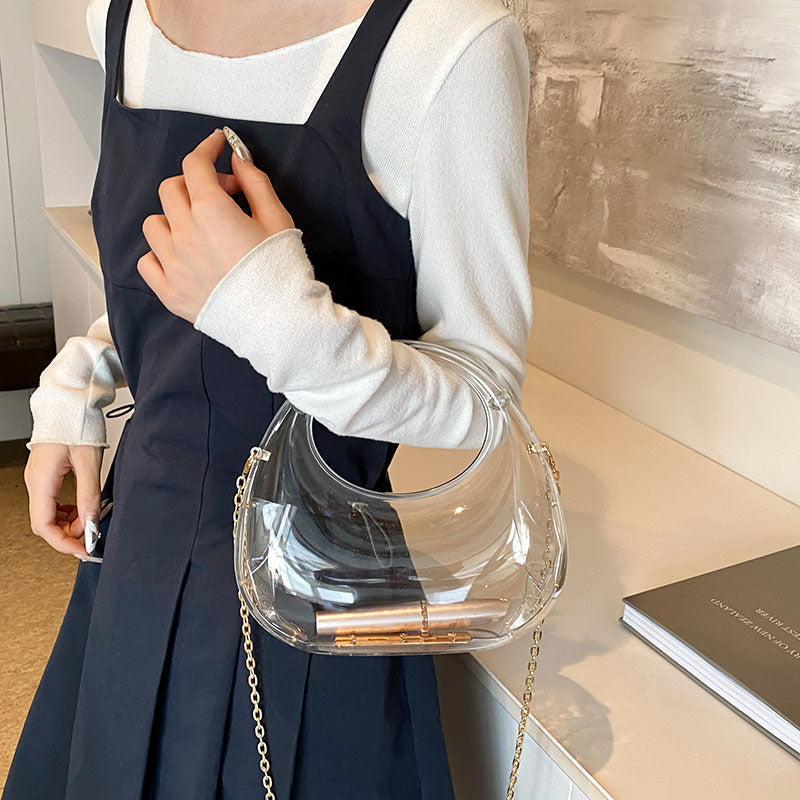 Front view of the Golden Eclipse handbag in a transparent finish. The bag has a unique crescent shape with a large circular handle cutout and a delicate gold chain strap. brand baazuu