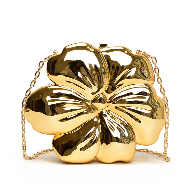 The Baazuu Bloom Bling floral clutch in a metallic gold finish. This sculptural, flower-shaped handbag features a hard-shell design and a chain strap, perfect as a modern statement piece.