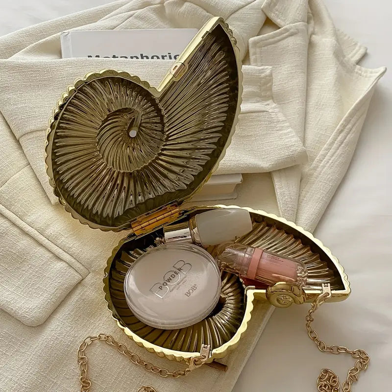 The Baazuu Auréelle conch bag. This unique, shell-shaped clutch features a sculptural, spiral design in a metallic gold finish with a chain strap, perfect as an artistic statement piece.