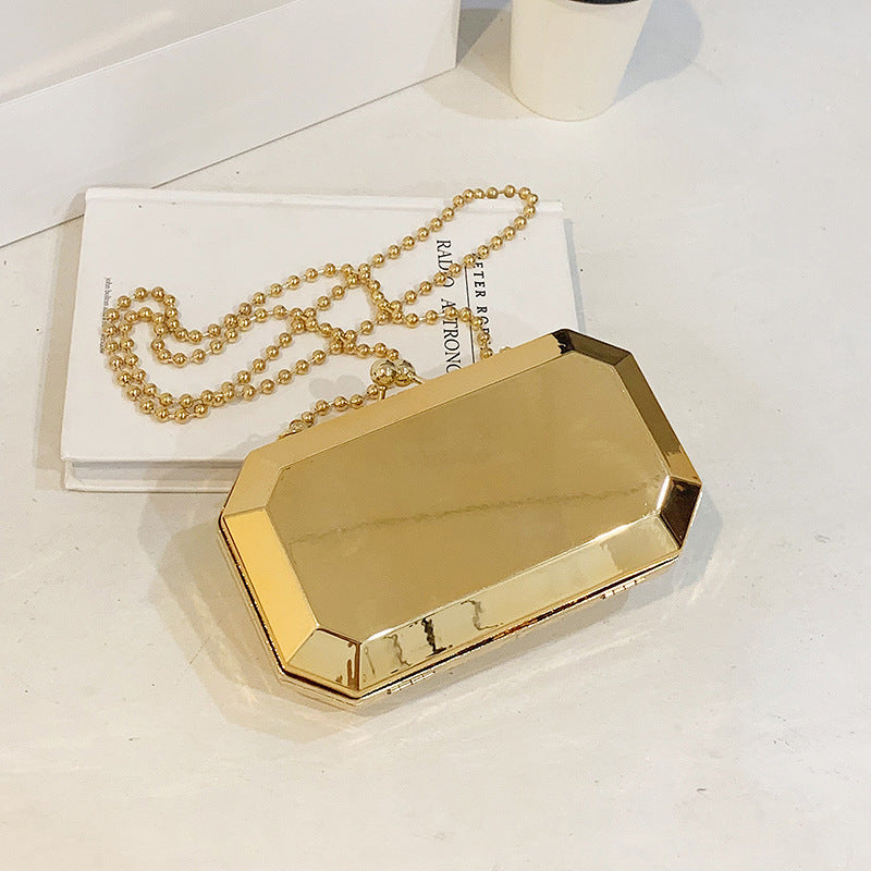 The Baazuu Golden Phantom box clutch in gold. This modern, octagonal evening bag features a minimalist, geometric design in a hard-shell metallic finish, complete with a chain strap.