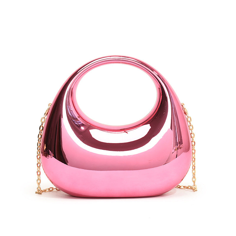 Front view of the Golden Eclipse handbag in a metallic pink finish. The bag has a unique crescent shape with a large circular handle cutout and a delicate gold chain strap. brand baazuu