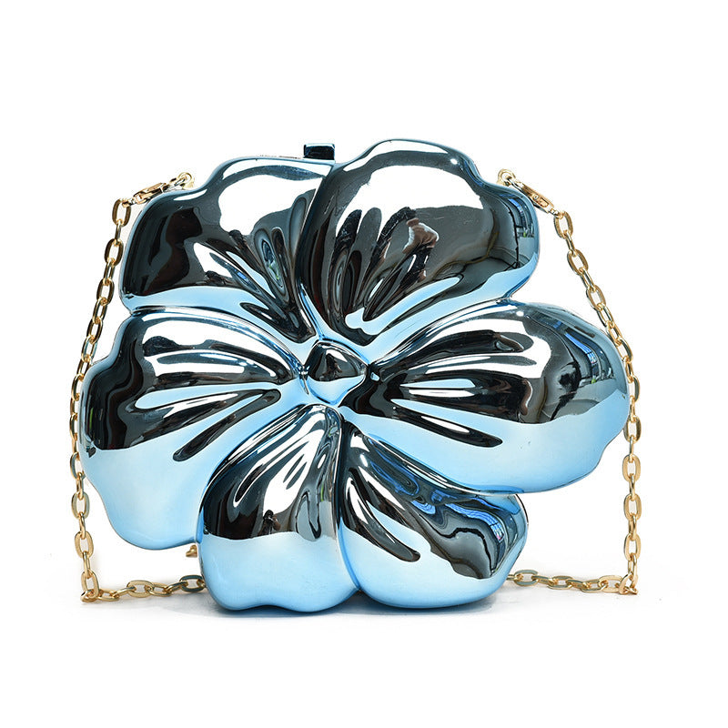 The Baazuu Bloom Bling floral clutch in a metallic blue finish. This sculptural, flower-shaped handbag features a hard-shell design and a chain strap, perfect as a modern statement piece.
