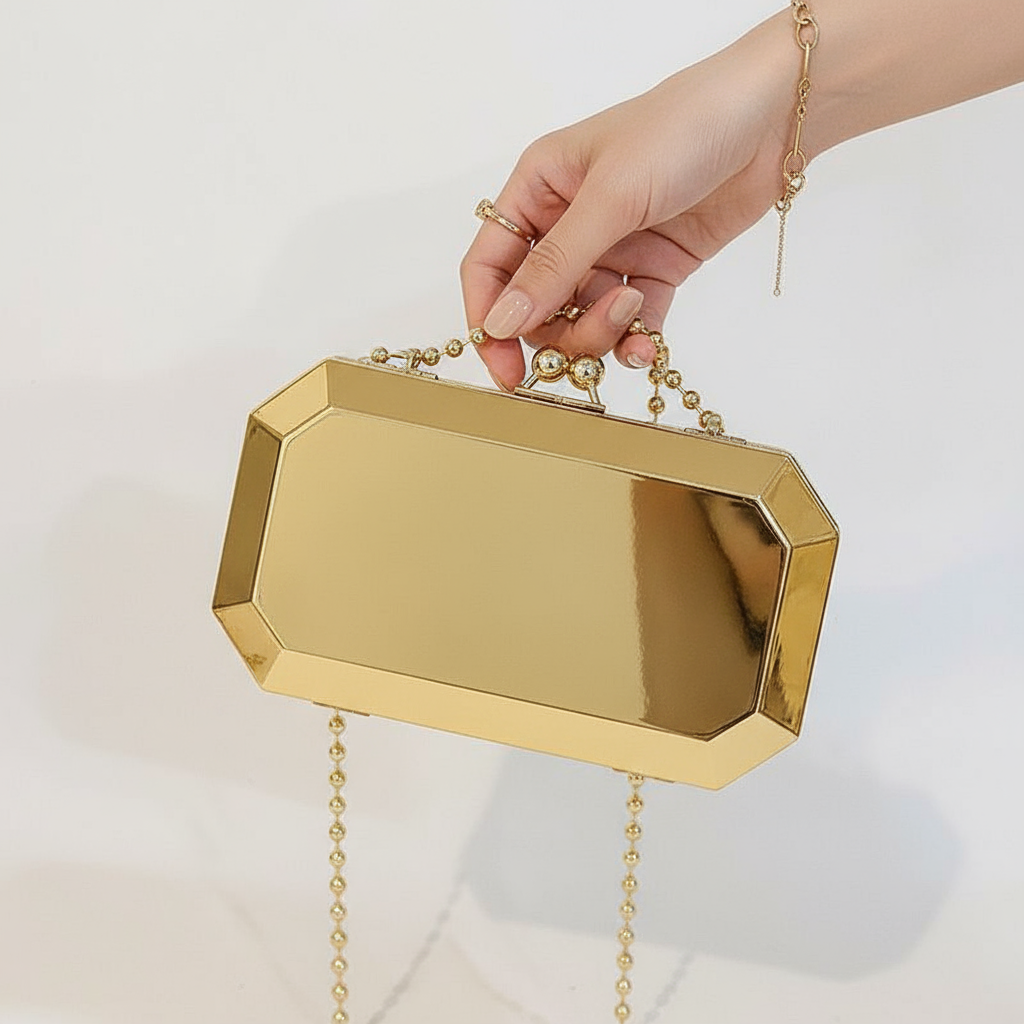 The Baazuu Golden Phantom box clutch in gold. This modern, octagonal evening bag features a minimalist, geometric design in a hard-shell metallic finish, complete with a chain strap.