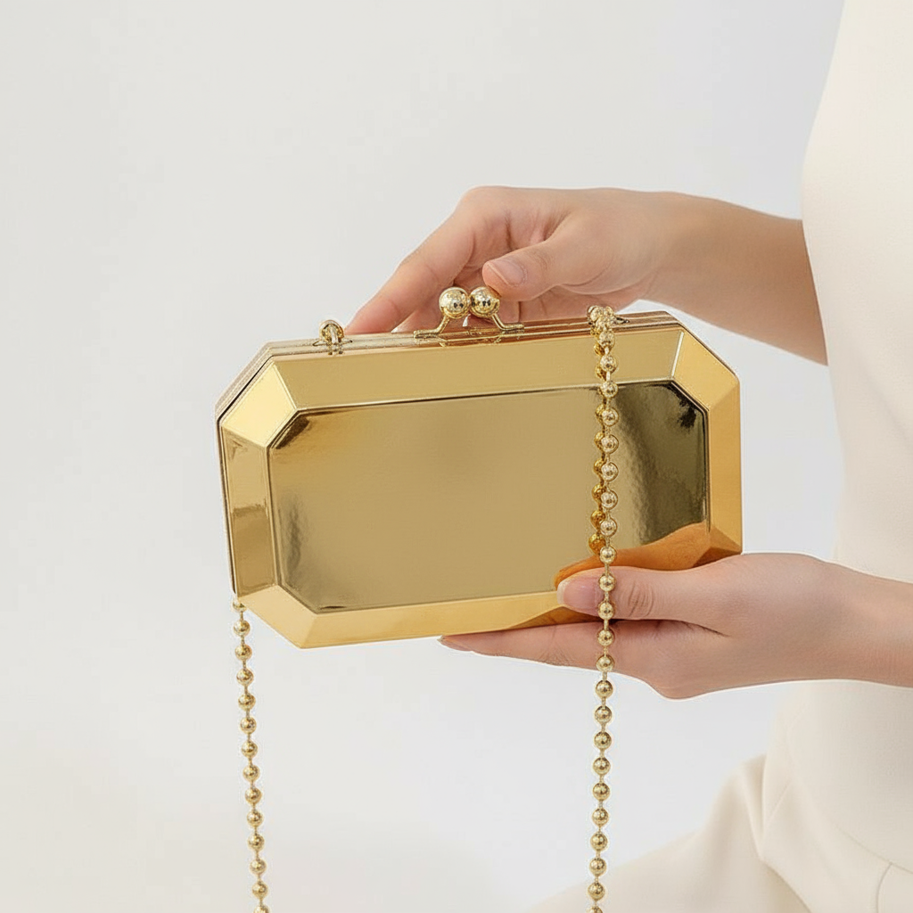 The Baazuu Golden Phantom box clutch in gold. This modern, octagonal evening bag features a minimalist, geometric design in a hard-shell metallic finish, complete with a chain strap.