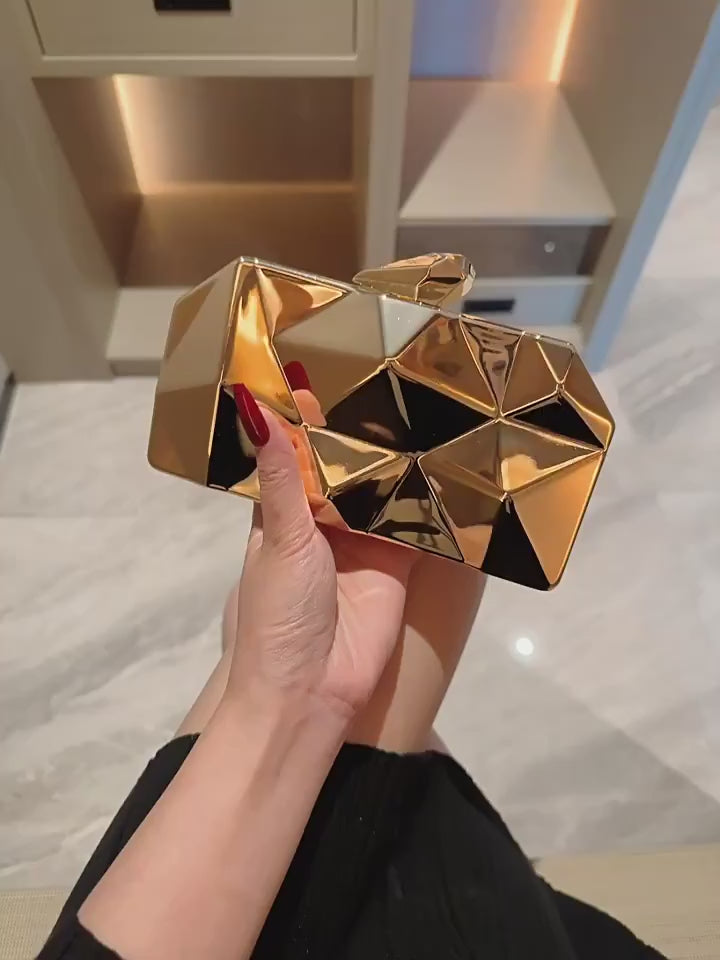The Prism Aura geometric acrylic clutch shown in gold color. This statement evening bag has a reflective, diamond-cut design and comes with a chain strap.