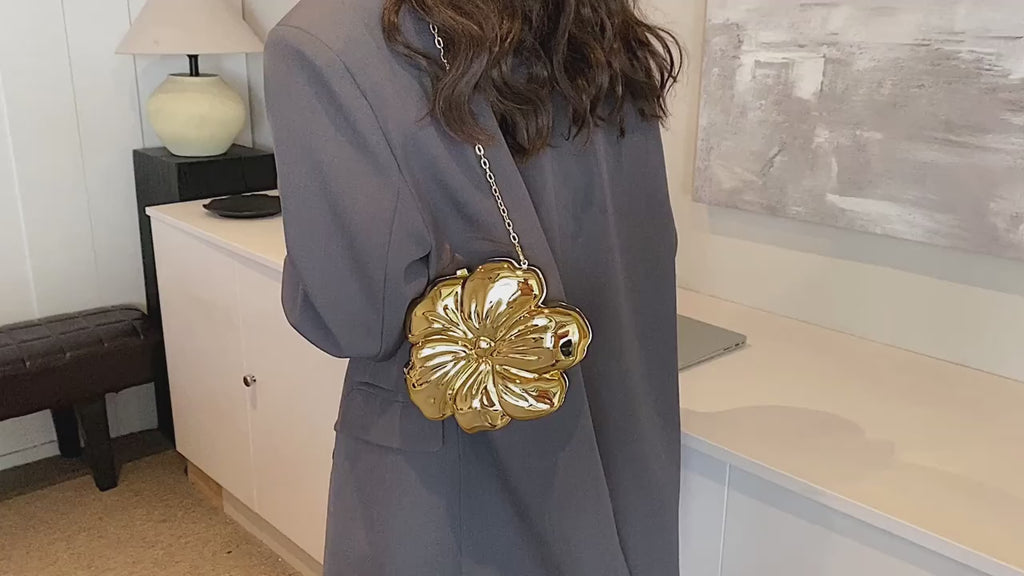 The Baazuu Bloom Bling floral clutch in a metallic gold finish. This sculptural, flower-shaped handbag features a hard-shell design and a chain strap, perfect as a modern statement piece.